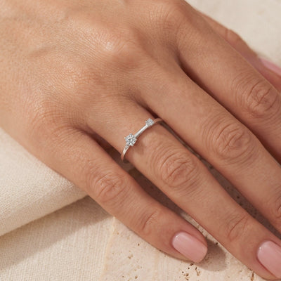 Silver asymmetric bypass ring with two prong-set clear stones, shown worn on a person's hand.