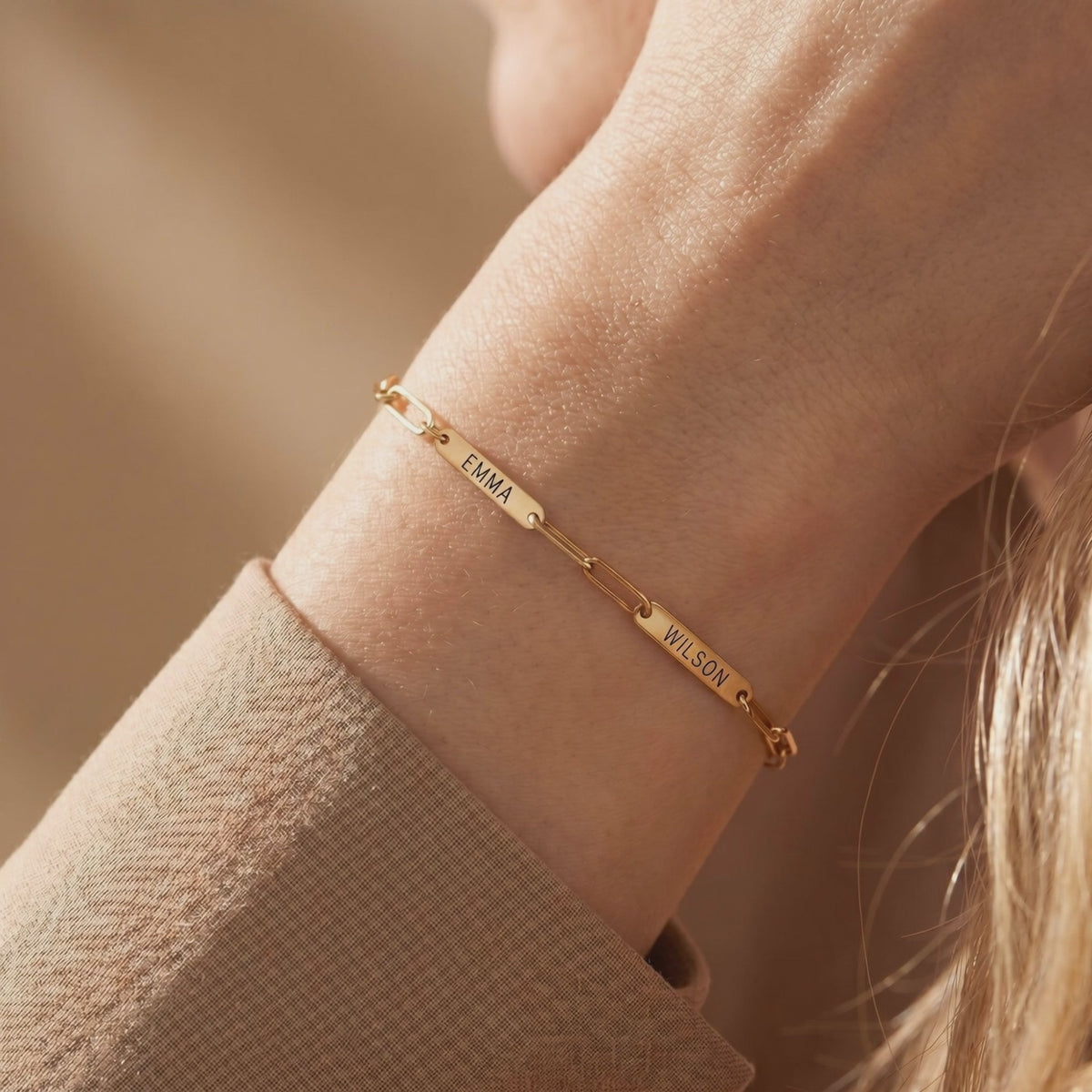 Gold-tone personalized link bracelet worn on a wrist, with engraved plates reading EMMA and WILSON.