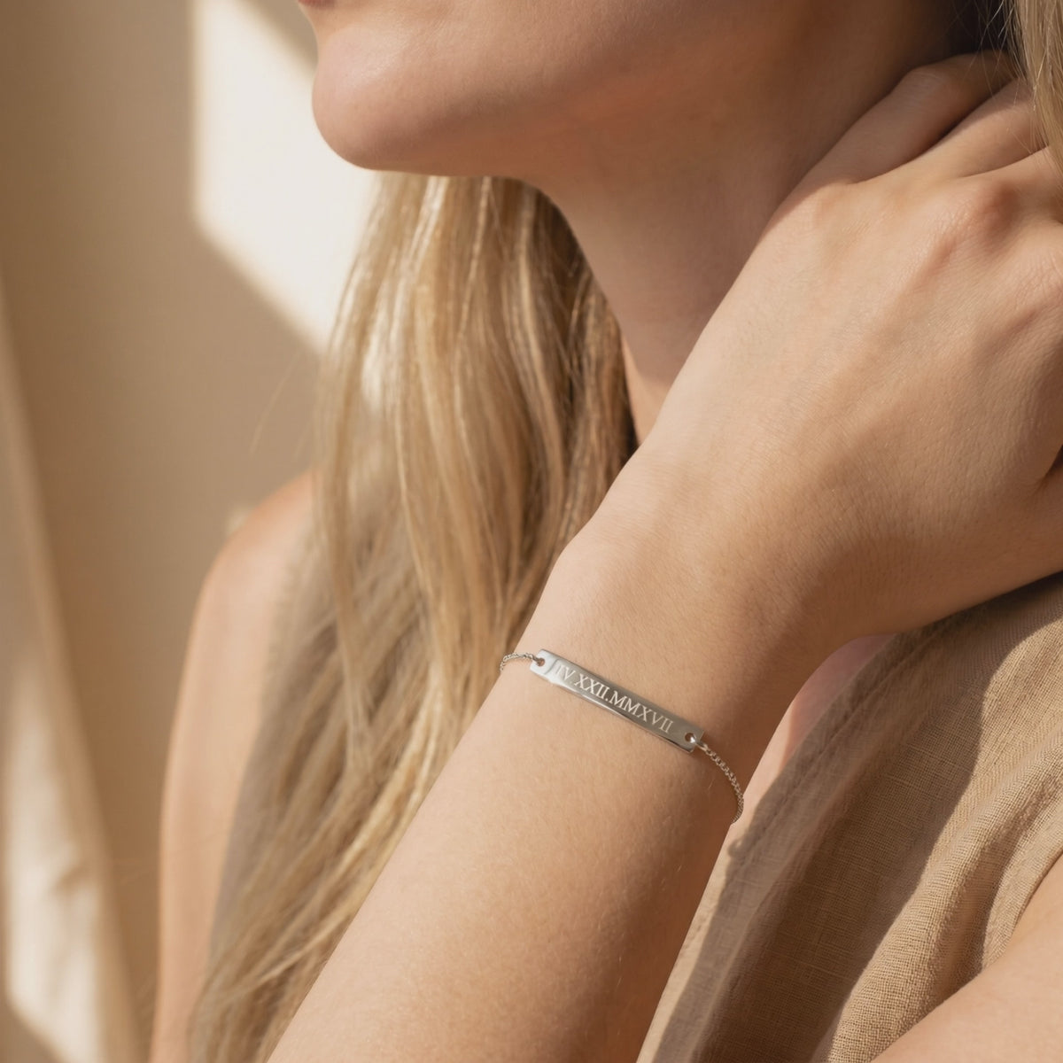 Silver-toned bar bracelet engraved with Roman numerals, worn on a woman's wrist.