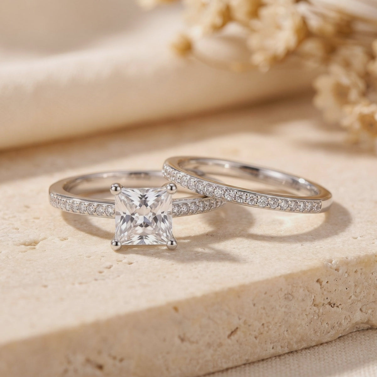 Silver ring set displayed on a stone surface, showing the princess-cut center stone and matching pavé band.