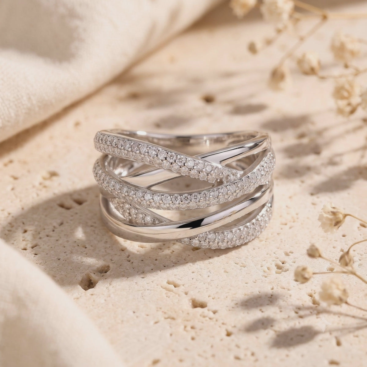 Silver multi-row crossover ring displayed on its side atop a textured stone surface
