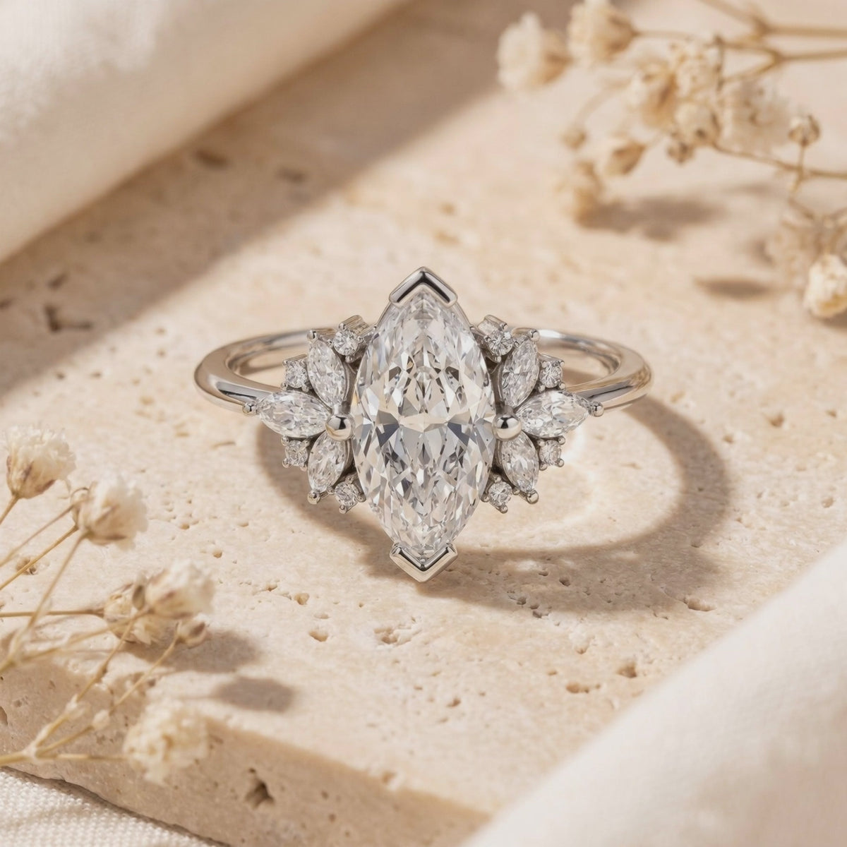 Close-up of a silver ring with a large marquise-cut moissanite and marquise-and-round side stones on beige stone.