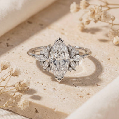 Close-up of a silver ring with a large marquise-cut moissanite and marquise-and-round side stones on beige stone.