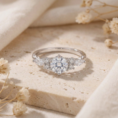 Close-up of the silver Claraluna ring with marquise and round side accents resting on a beige stone surface.