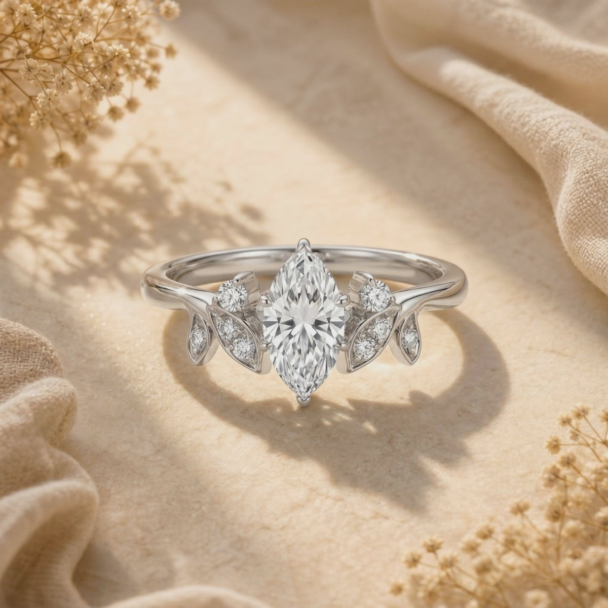 Front-facing close-up of a silver marquise-cut moissanite ring with leaf-shaped side accents on fabric