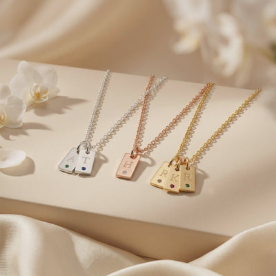 Silver, rose gold-tone, and gold-tone necklaces displayed on a cream platform, with tags engraved A, T, H, R, K, and R.