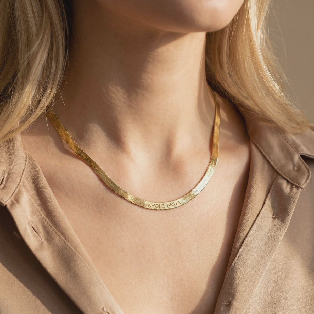 Gold-toned flat herringbone chain necklace engraved with KHLOE ANNA, shown worn around a woman's neck.
