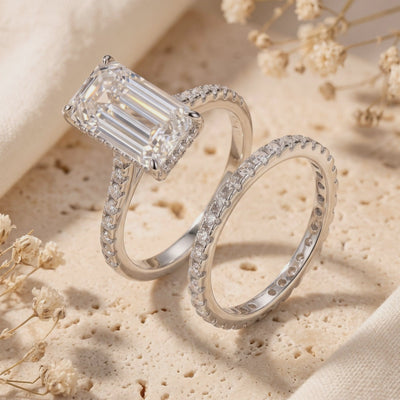 Silver ring set with an emerald-cut stone and matching pavé band displayed upright on a stone slab.