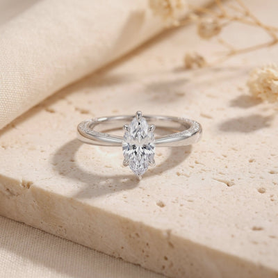 Close-up of a silver ring with a marquise-cut clear center gem displayed upright on a beige stone surface.