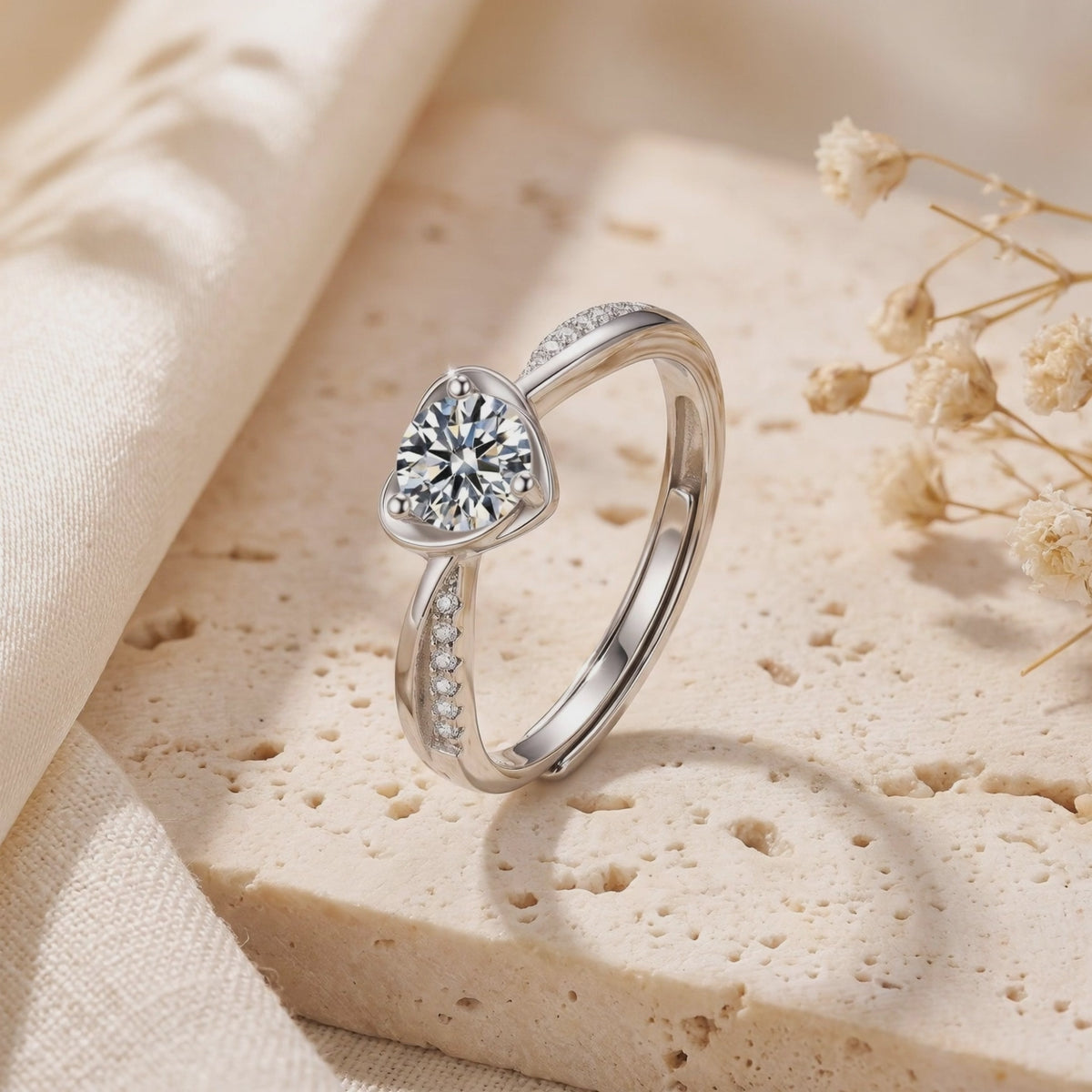 Silver heart-bypass ring with a round center gem and pave accents, standing on a textured stone surface.