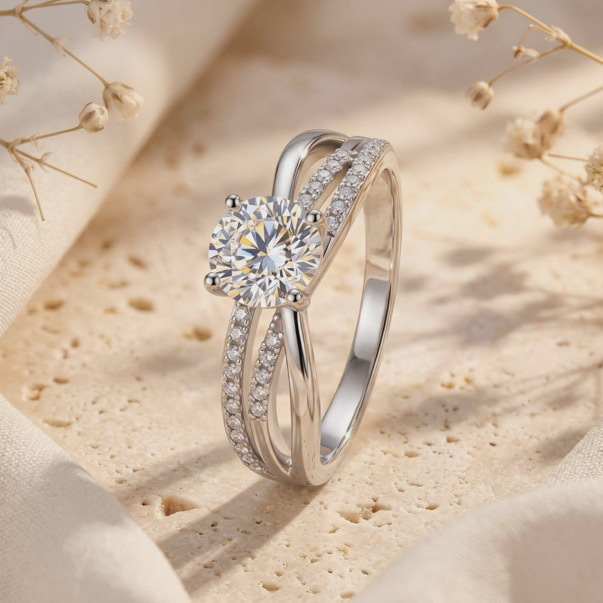 Close-up of a silver crossover ring with a round center stone and pavé bands on a beige stone backdrop.