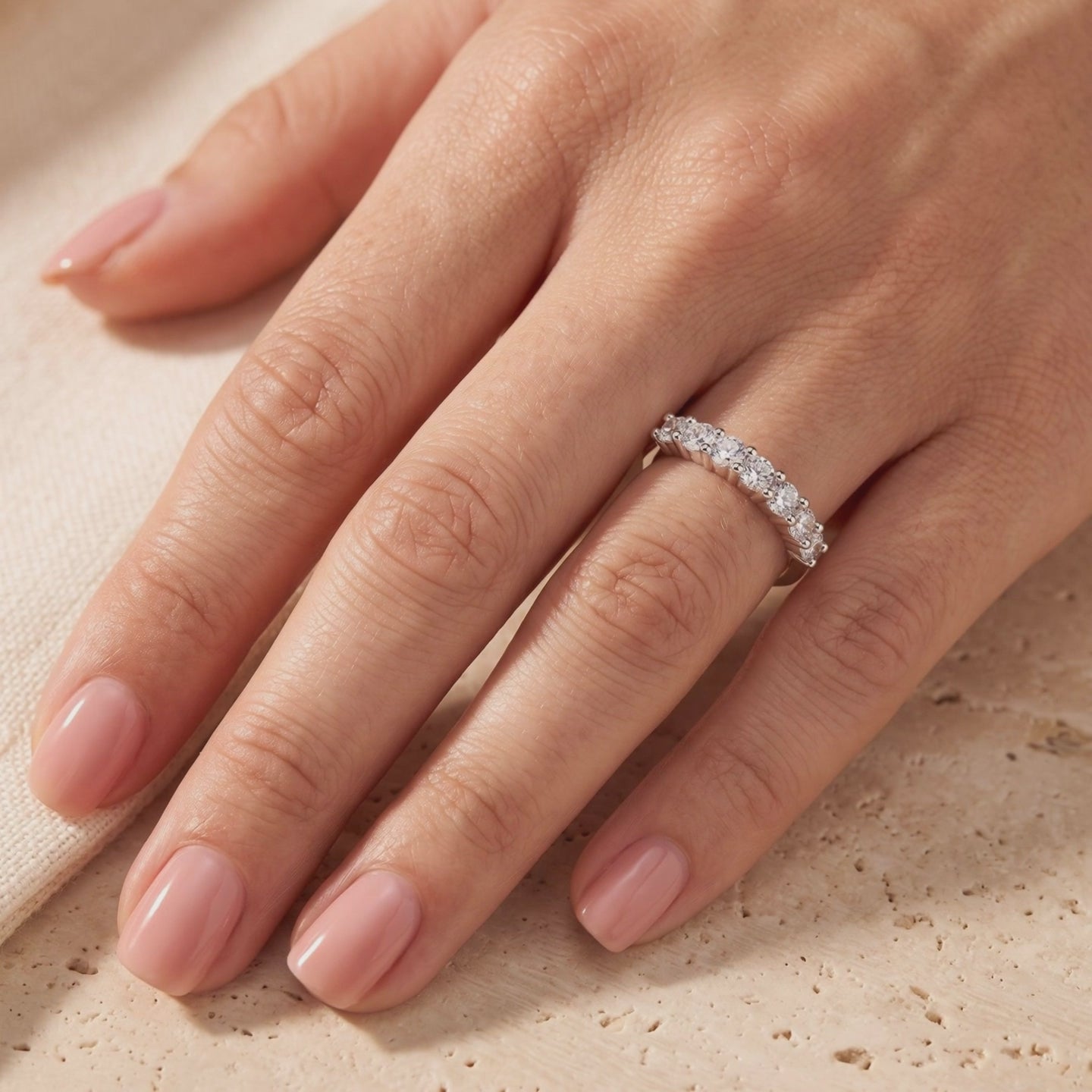 Preview frame of a silver ring set with seven round clear stones worn on a hand against a beige surface.