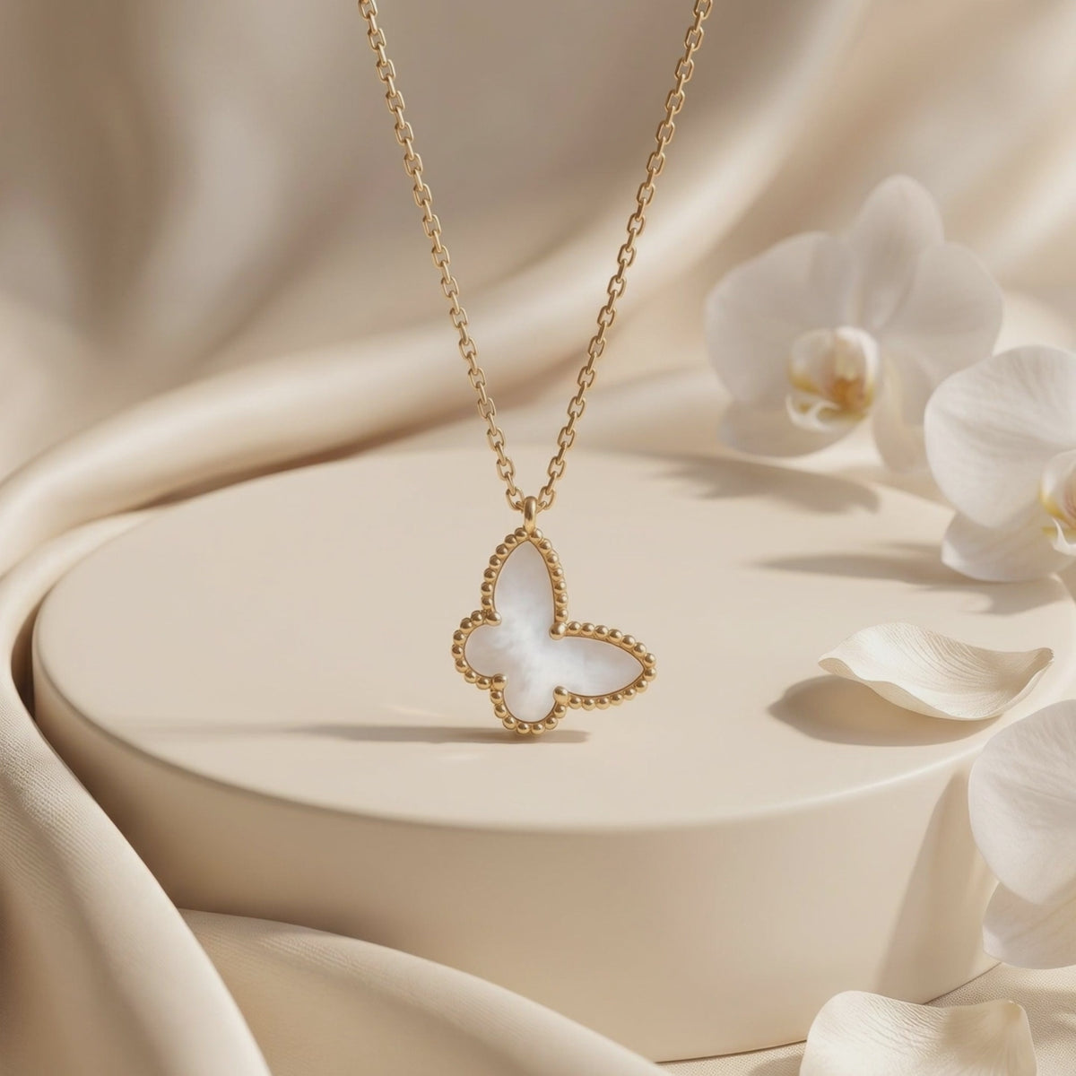 Mother-of-pearl butterfly pendant necklace displayed on a beige pedestal surrounded by white orchids.