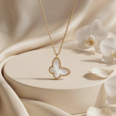 Mother-of-pearl butterfly pendant necklace displayed on a beige pedestal surrounded by white orchids.
