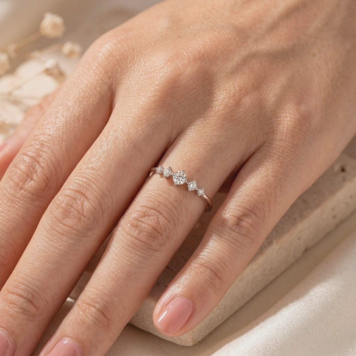 Elysand silver ring with five graduated moissanite stones worn on a hand, with dried flowers in the background.