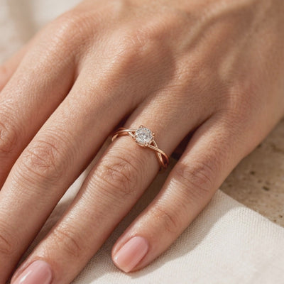 Rose gold-toned Calydonia ring with a twisted band and round center stone, shown worn on a hand.