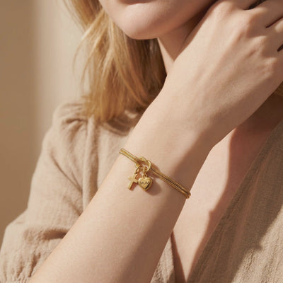 Gold-tone double snake-chain bracelet worn on a wrist, with a knotted center and cross and MUM heart charms.