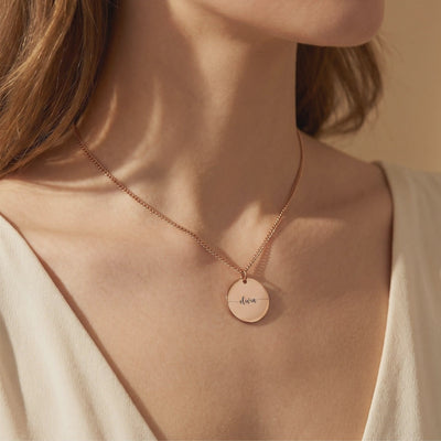 Rose gold-colored Eloise necklace worn on a model, with a round disc pendant engraved “olivia.”