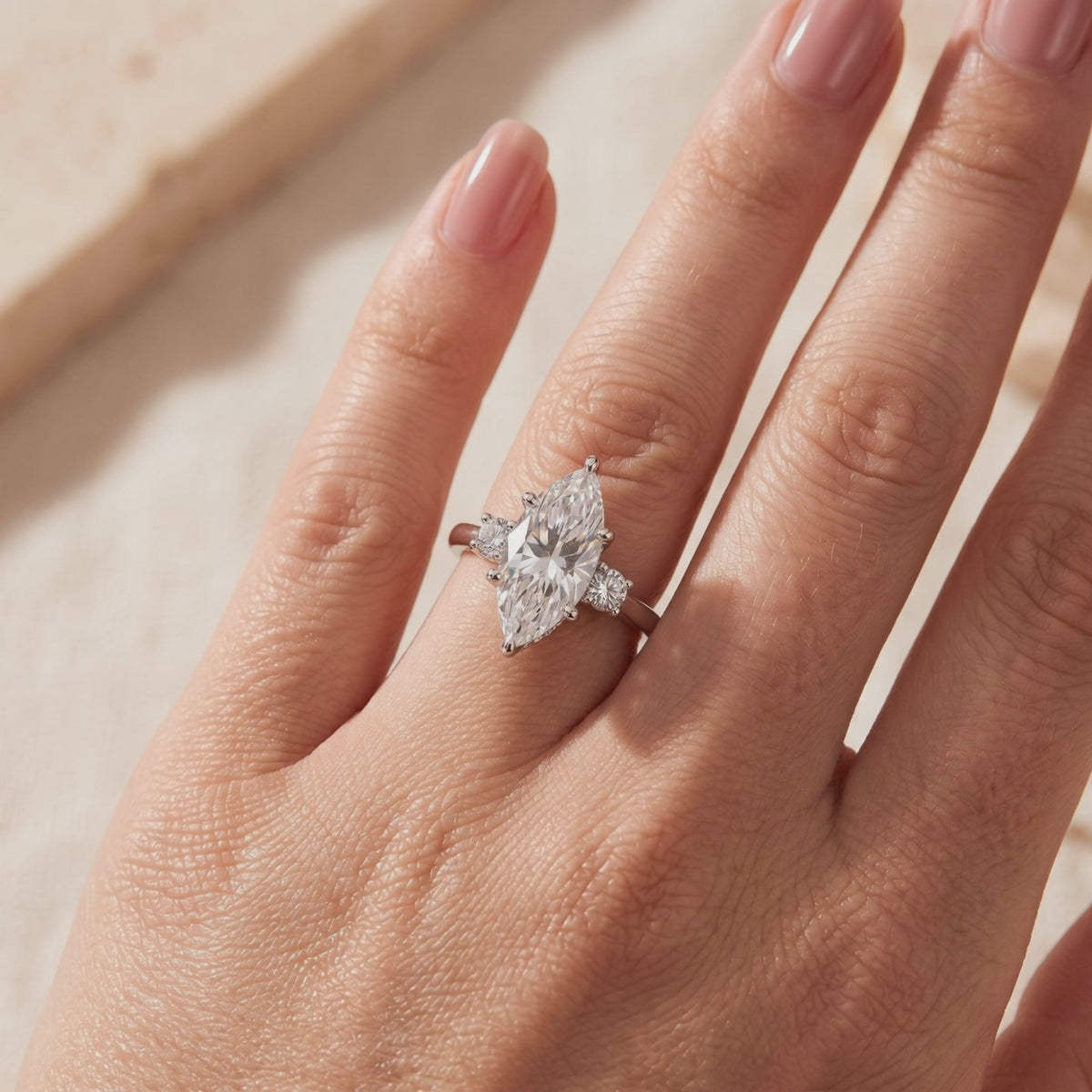 Silver three-stone ring with a marquise center stone and round accents, worn on a hand.
