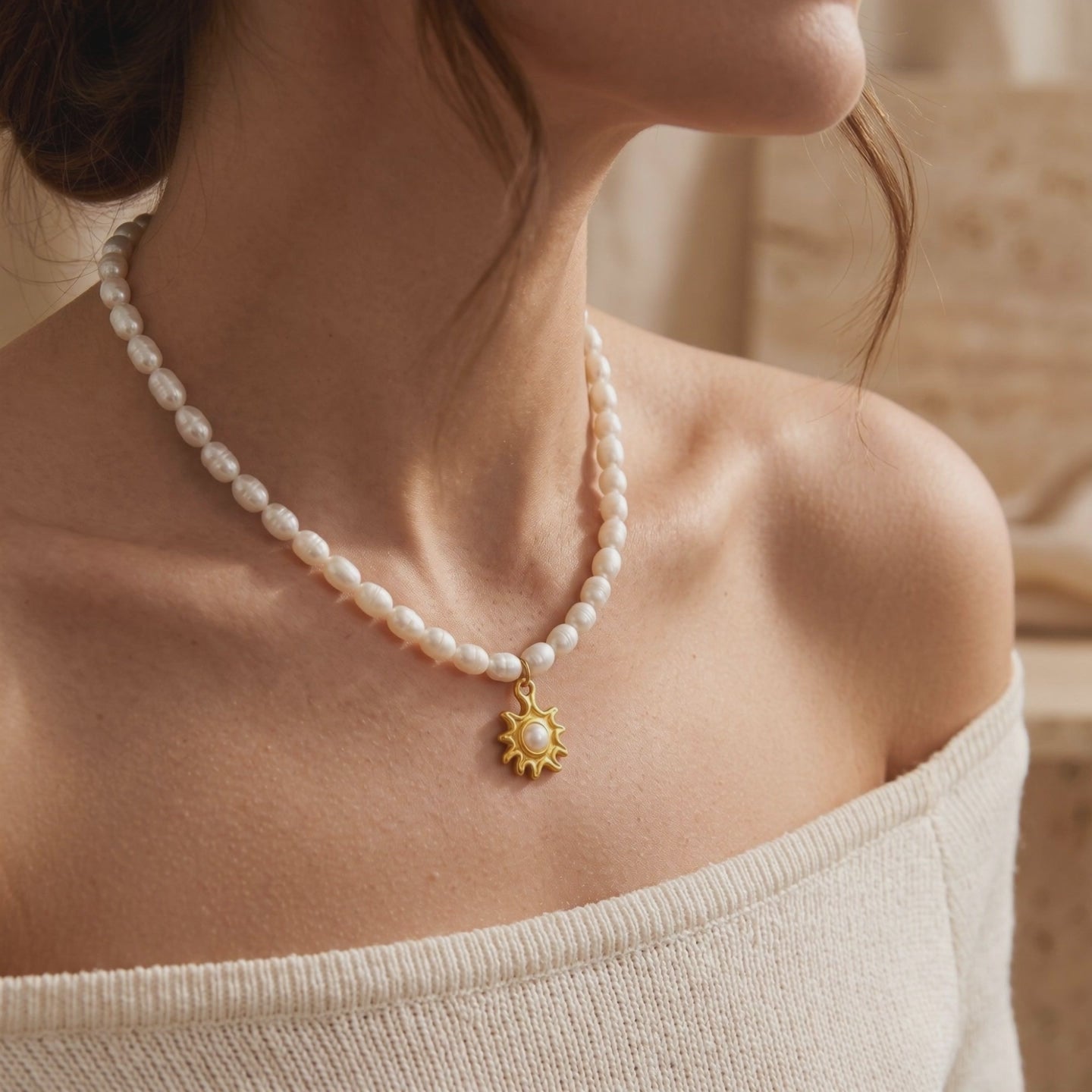 Model wearing a pearl strand necklace with a gold-tone sunburst pendant and center pearl.