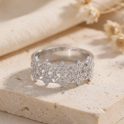 Silver ring with repeating snowflake motifs and clear stones displayed upright on a beige textured tile.