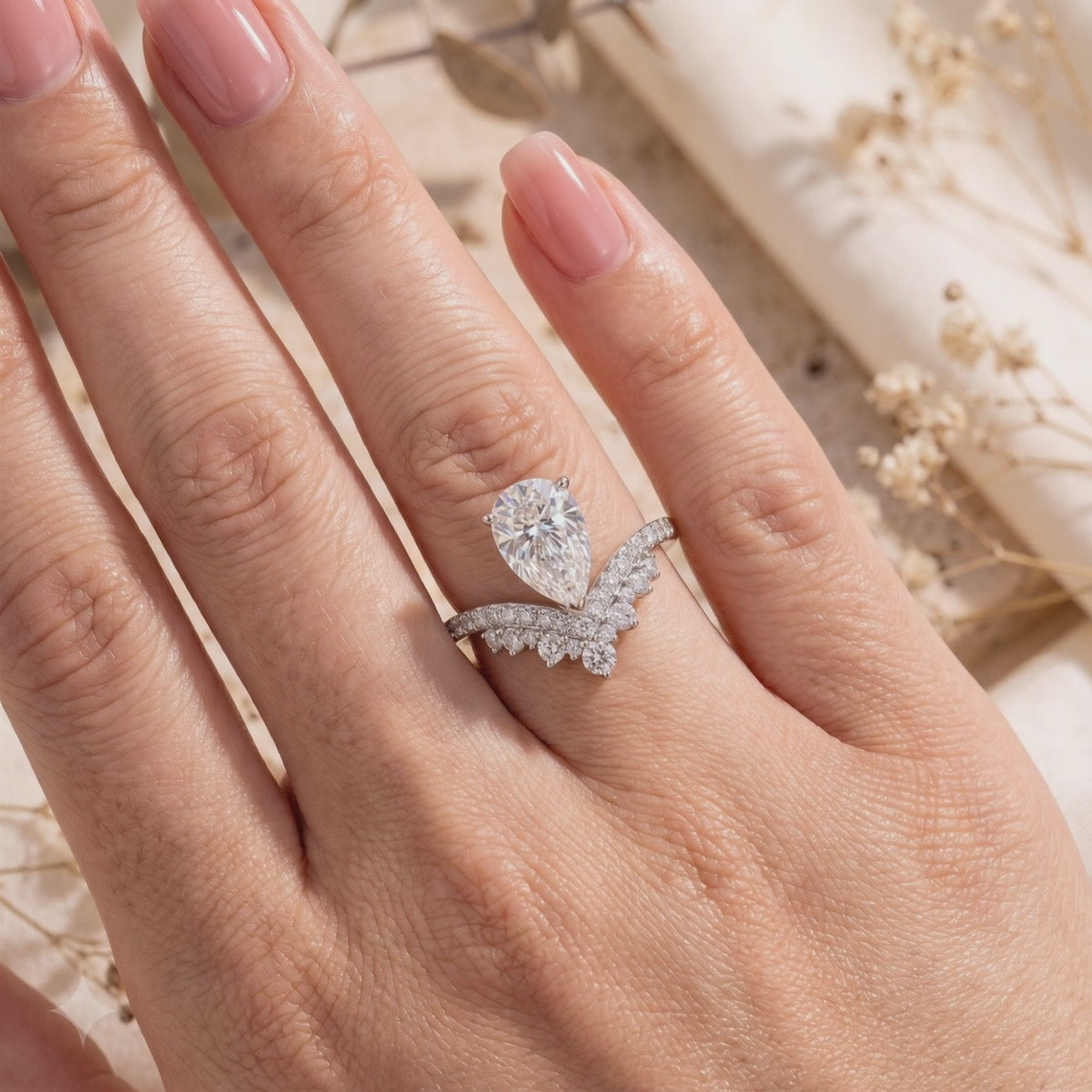 Worn on a hand, a silver wishbone ring shows a pear-cut center stone and nested micro-pavé bands.