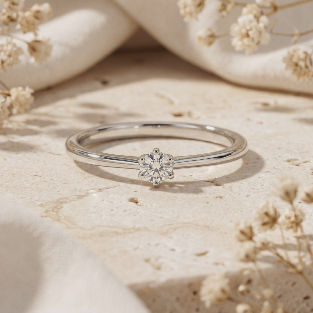 Close-up of the silver round moissanite solitaire ring on a stone surface with dried flowers.