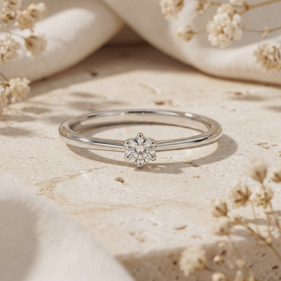 Close-up of the silver round moissanite solitaire ring on a stone surface with dried flowers.