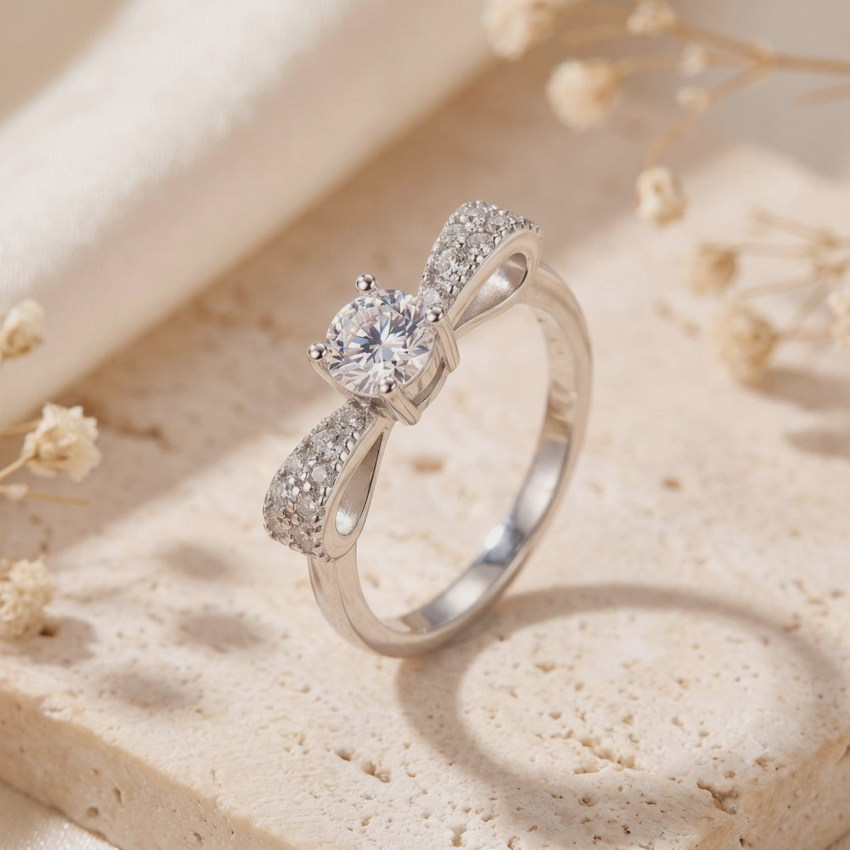 Silver bow ring with pavé-set loops displayed upright on a beige stone surface.