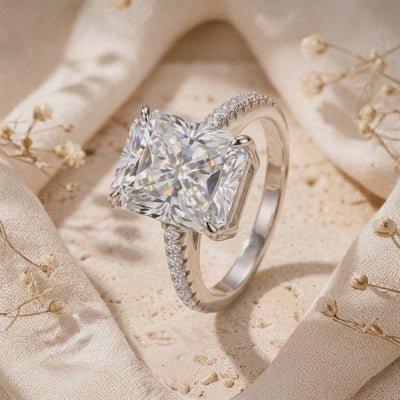 Close-up of the silver ring standing on folded fabric, showing its radiant-cut clear center stone and pavé band.