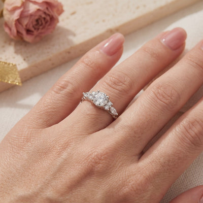 The Carlotta silver ring with a round center stone and marquise accents, shown worn on a finger beside a dried rose.