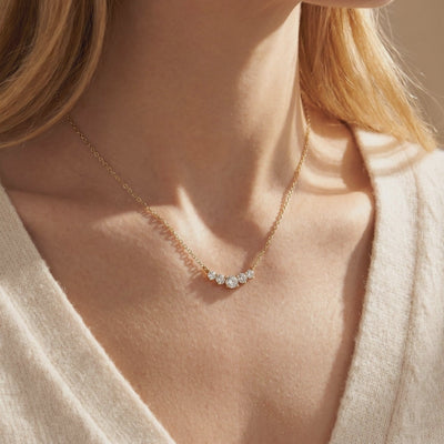 Gold-tone necklace with five round clear stones in a curved arc, shown worn at a model's collarbone.
