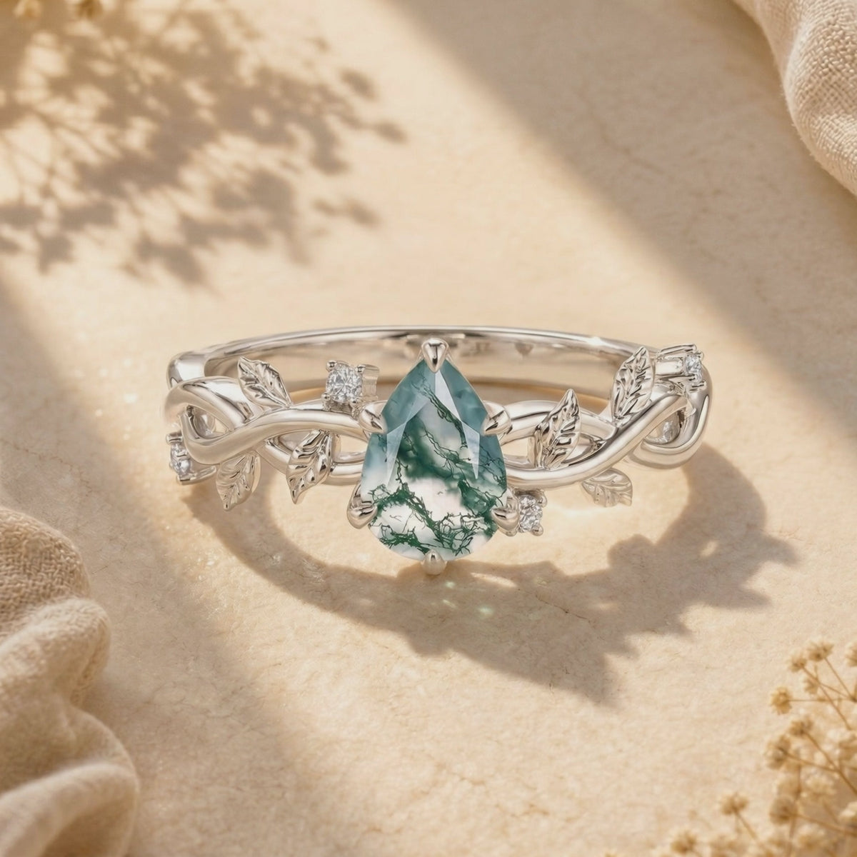 Close-up of a silver ring featuring a pear-cut green moss agate stone on a leafy vine band with accent gems.
