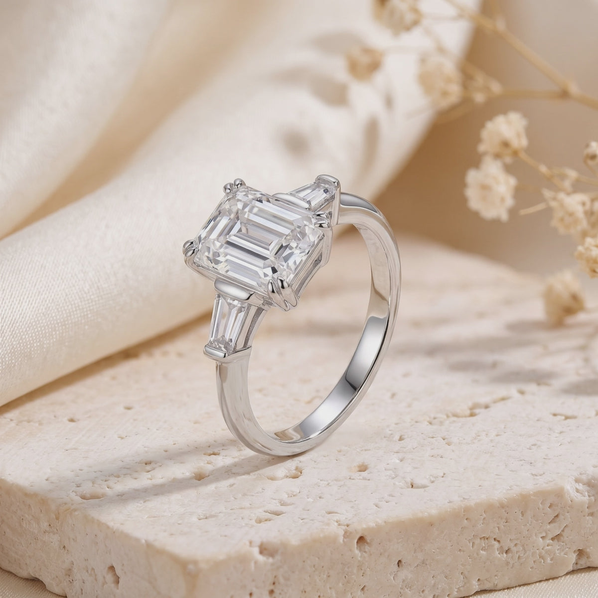 Video preview of a silver emerald-cut three-stone ring displayed upright on a textured stone block.