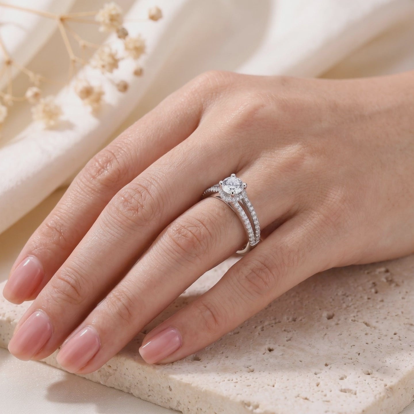 Silver split-shank ring with a round clear center stone, worn on a hand over a textured stone surface.
