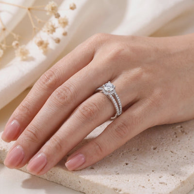 Silver split-shank ring with a round clear center stone, worn on a hand over a textured stone surface.