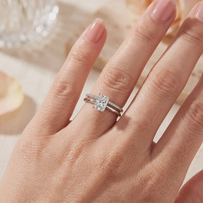 Stacked silver-tone ring set worn on a finger, with an emerald-cut clear center stone and pavé accent band