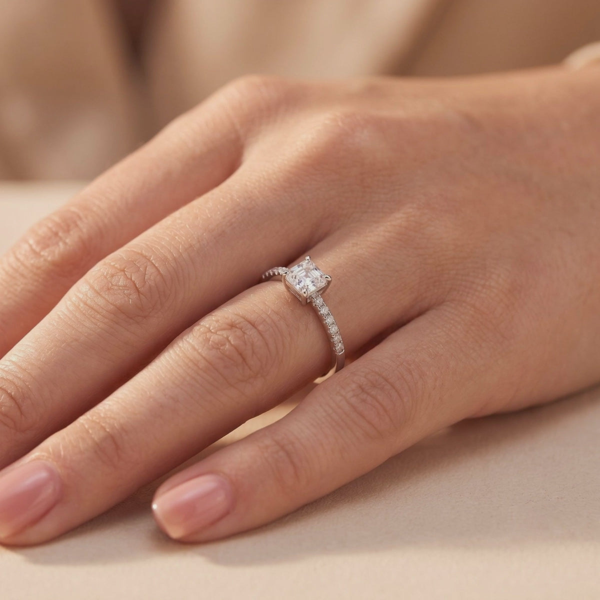 Angled view of the silver ring worn on a hand, showing its square center stone and pavé-set band.