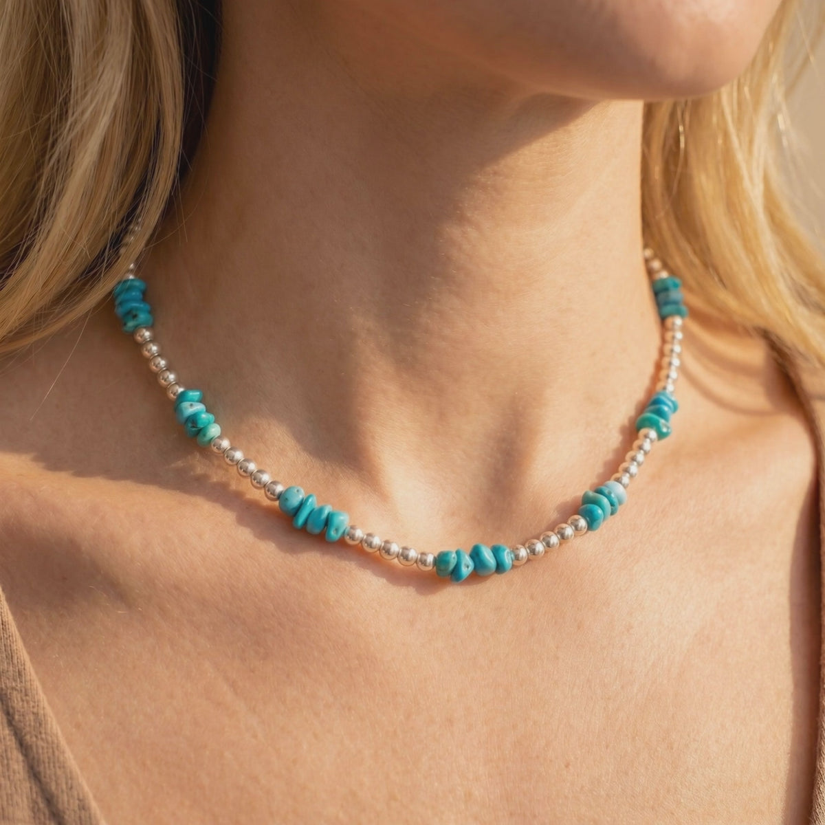 Close-up of a turquoise and silver-bead necklace worn around a woman’s neck at the collarbone.