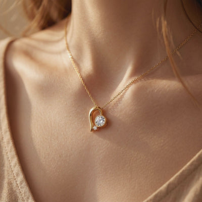 Close-up of a person wearing a gold-tone abstract heart pendant necklace with large and small round moissanite stones.