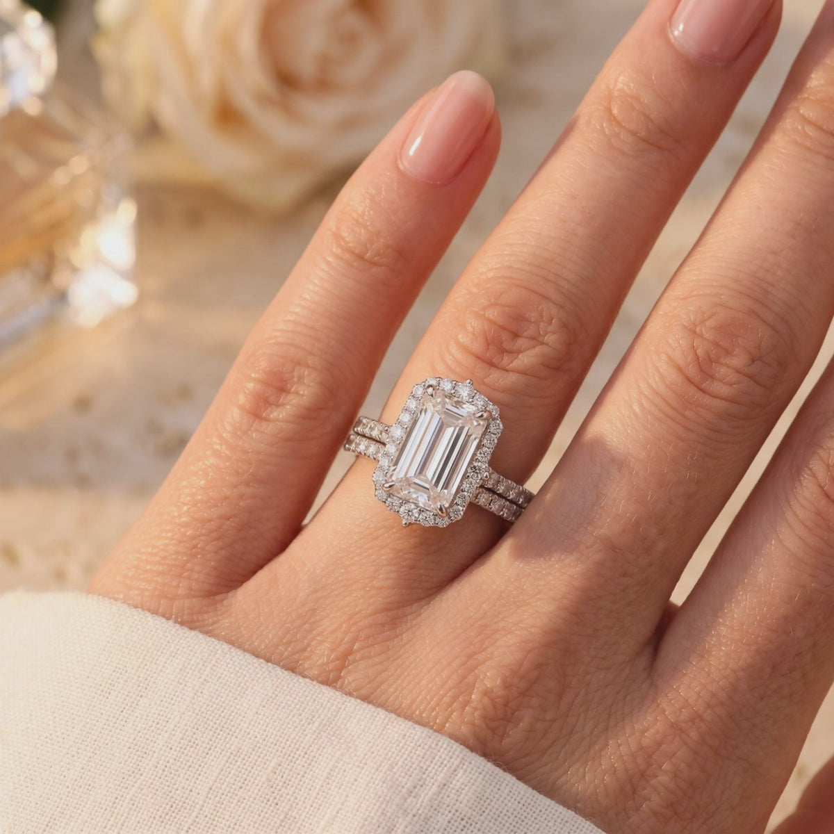Silver-tone double ring set with a halo emerald-cut center stone worn on a hand.