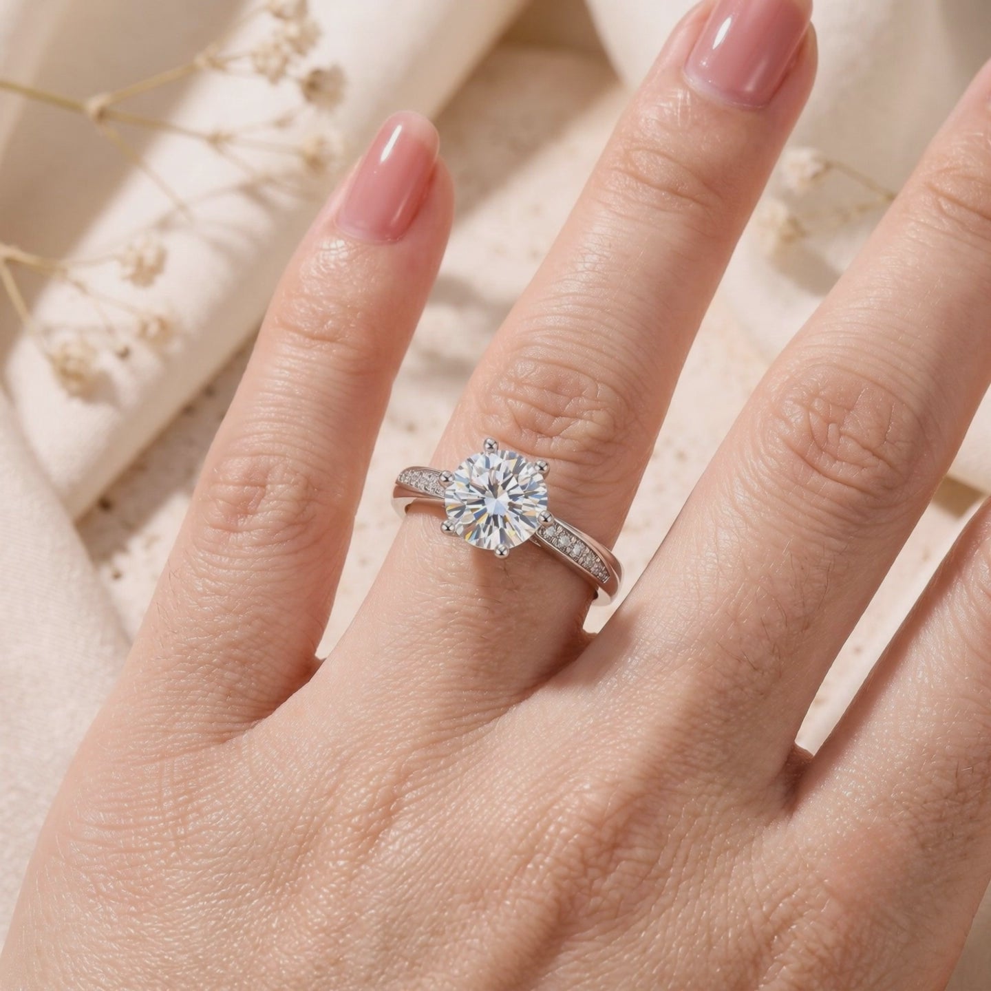 Silver solitaire ring worn on a finger, with a round clear center stone and pavé accents on the tapered band.