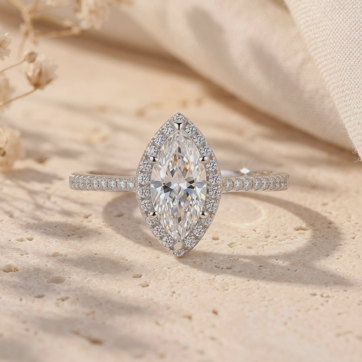 Front close-up of a silver marquise halo ring with a clear center gem on a textured stone surface.