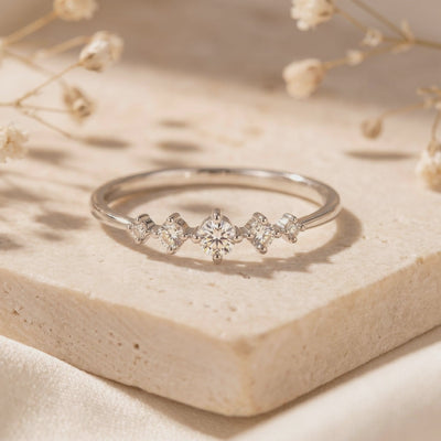 Silver ring with five graduated round moissanite stones displayed on a pale textured stone block.