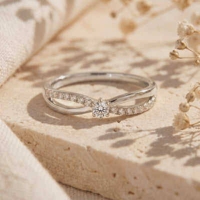 Silver-toned bypass ring with a round center stone and pavé accents, resting on a beige textured surface.