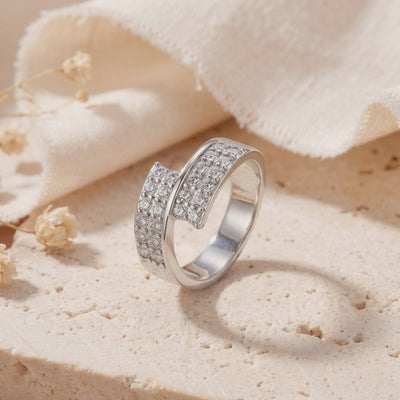 Silver bypass ring with pavé clear stones displayed upright on a textured stone surface.