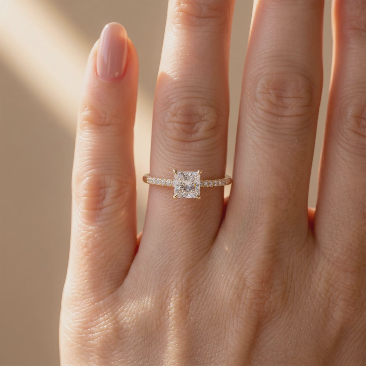 Princess-cut moissanite solitaire ring with a pavé band, shown worn on a hand.