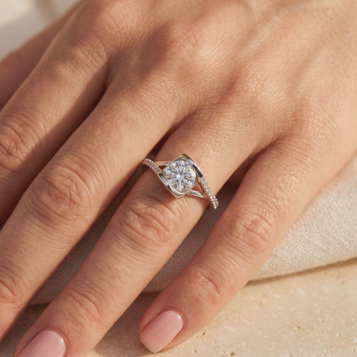 Close-up of a silver-tone bypass ring with a round clear center stone and pavé accents, worn on a hand.