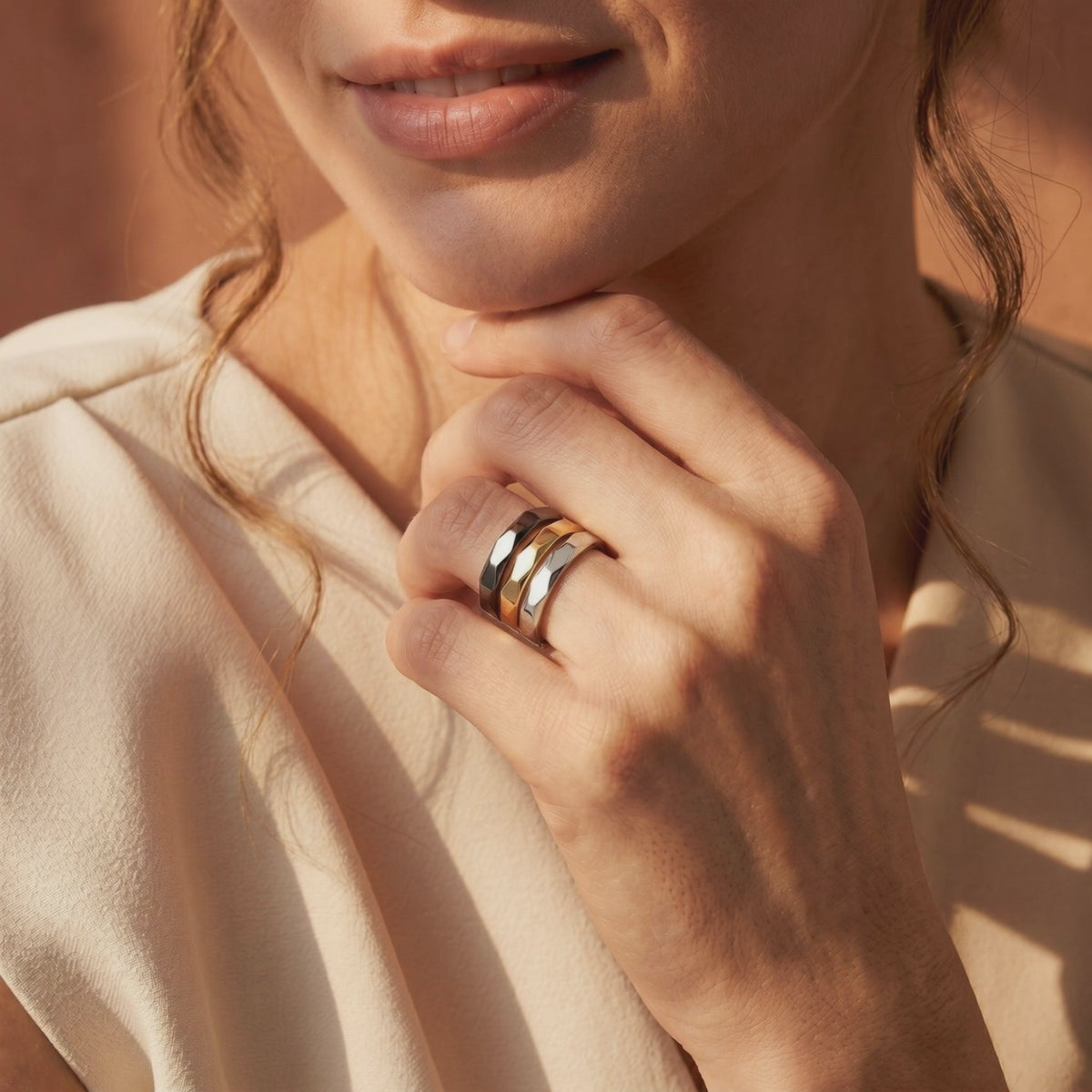 Model wearing three stacked faceted bands in black, gold-tone, and silver-tone.