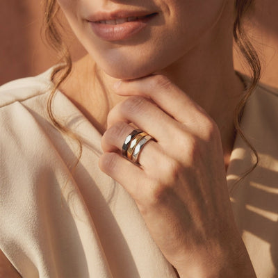 Model wearing three stacked faceted bands in black, gold-tone, and silver-tone.